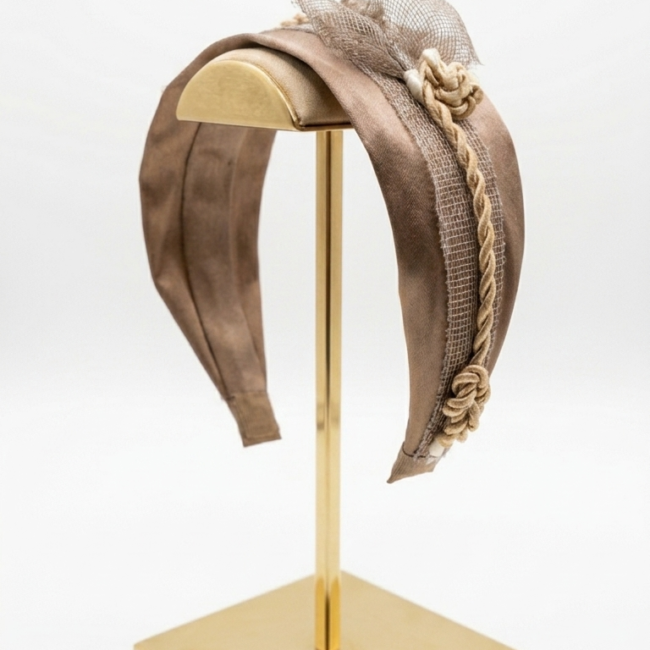 Exclusiva diadema de sinamay y satén marrón chocolate en expositor dorado.