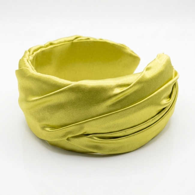 Primer plano de diadema ancha de satén verde lima con nudo central para invitada de boda.