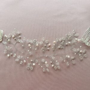 Tocado de novia artesanal de pedrería extendido con perlas naturales, cristales y estructura de hilo plateado sobre fondo rosa.